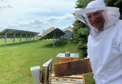 Beekeeper with equipment in front of solar panels