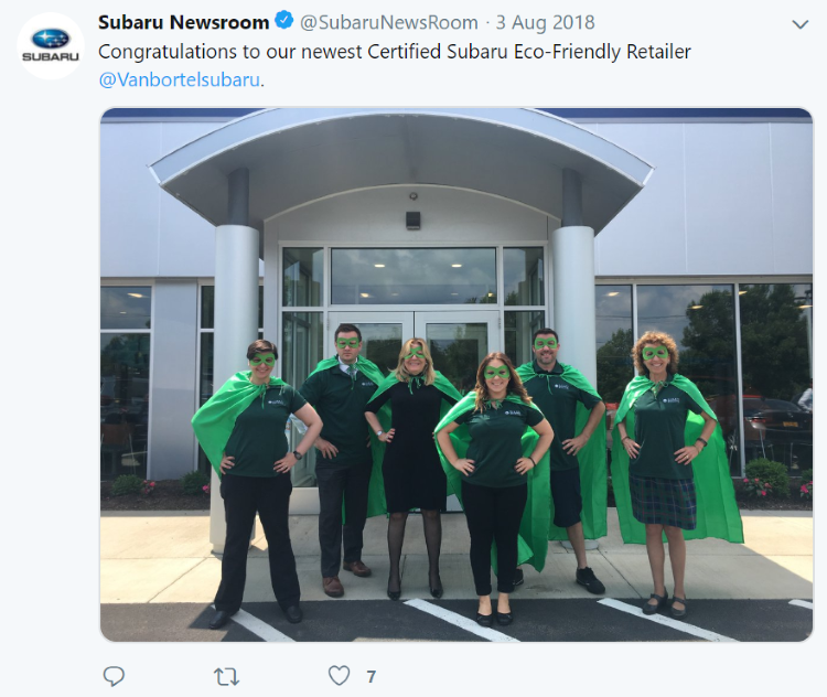 Van Bortel Subaru green team in capes in front of dealership