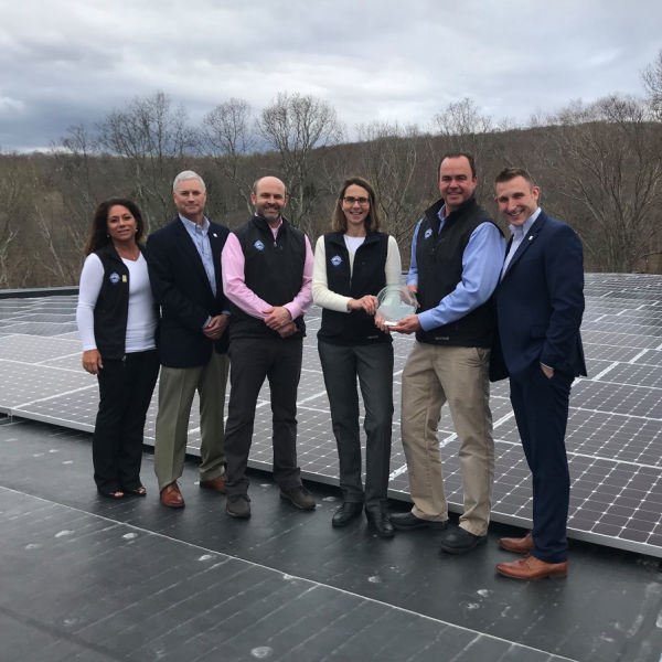 Subaru retailer employees accept trophy on top of roof covered in solar panels